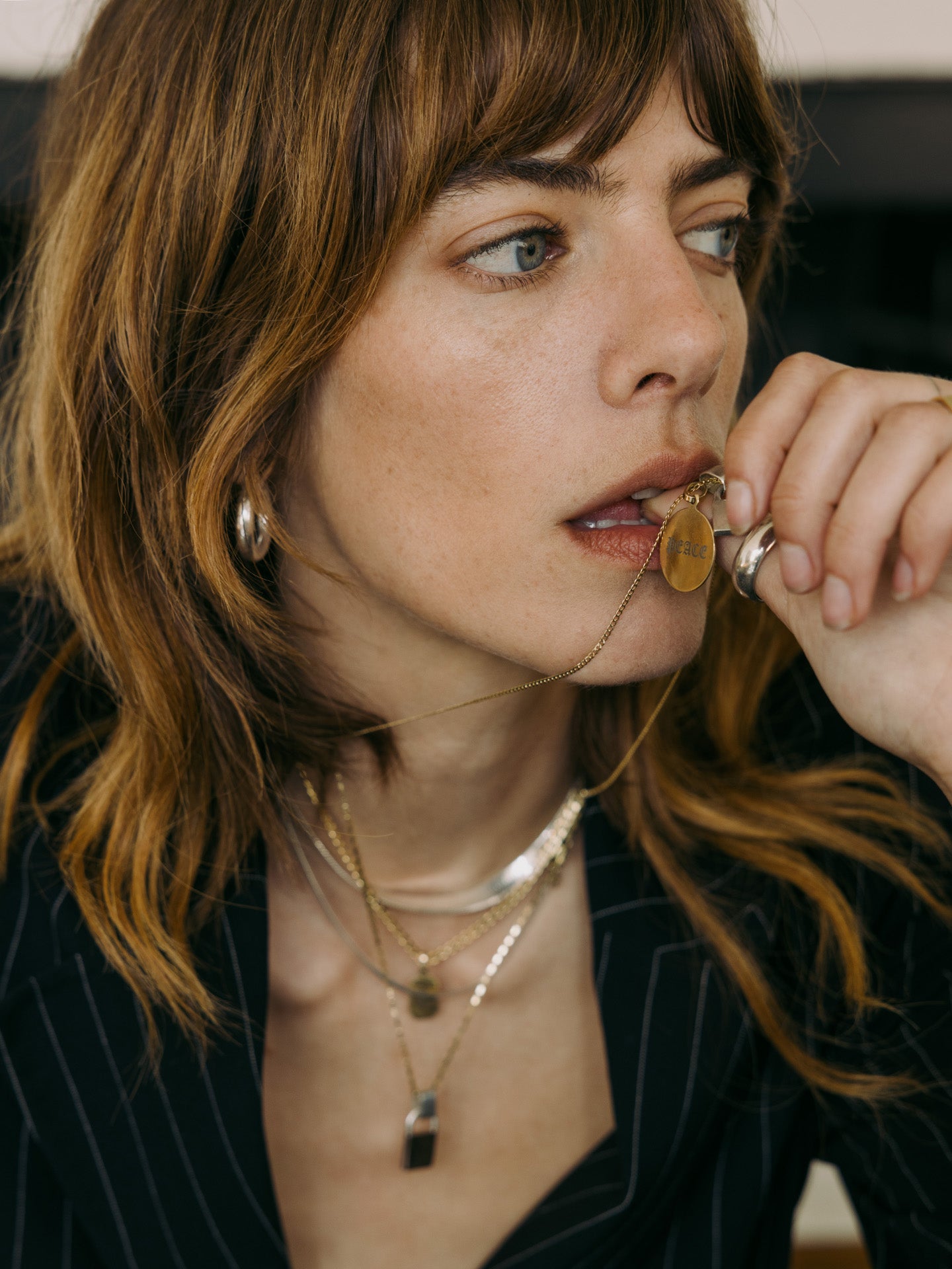 Disk Pendant engraved with 'Peace' strung on the Petite Havana Chain Necklace. Model is holding the pendant to her mouth. 