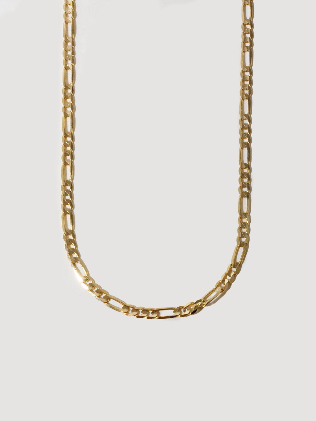 Close up of 14kt Yellow Gold Solid Figaro Chain Necklace pictured on light grey background.
