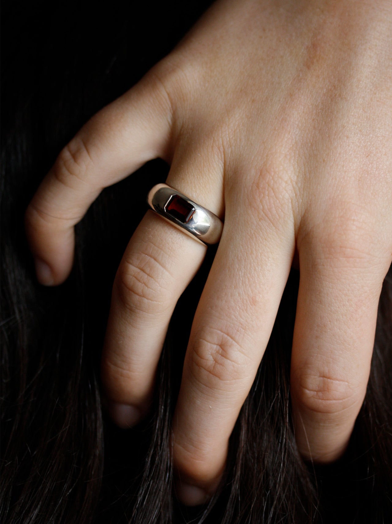 Close-up of a hand wearing a silver ring with a red stone on a dark background
