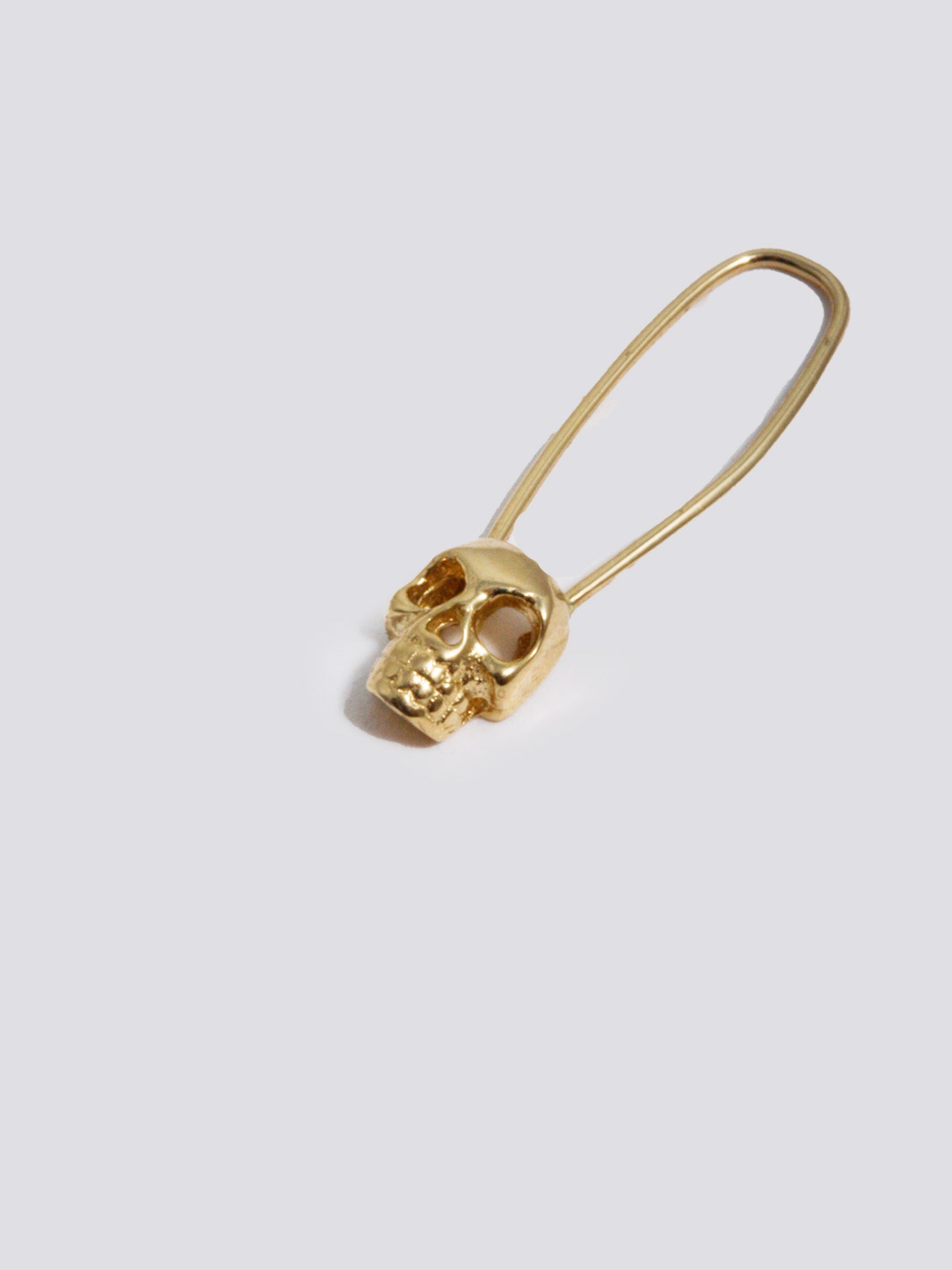 Product image of yellow gold safety pin with skull at base of pin, shot on white background. 