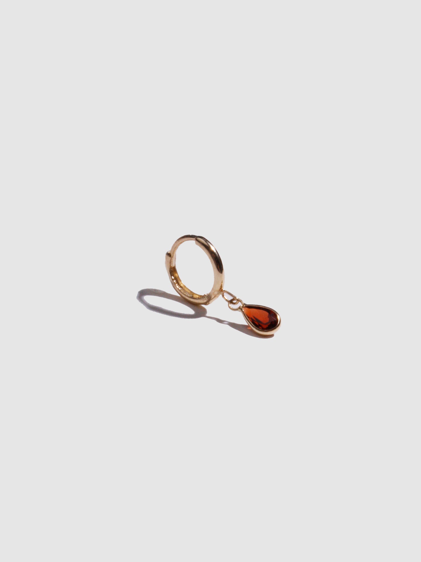 14kt Yellow Gold Gem Bezel Huggie pictured on light grey background. 