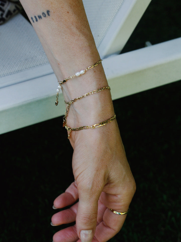 14kt Yellow Gold Solid Figaro Chain Bracelet pictured on models wrist.