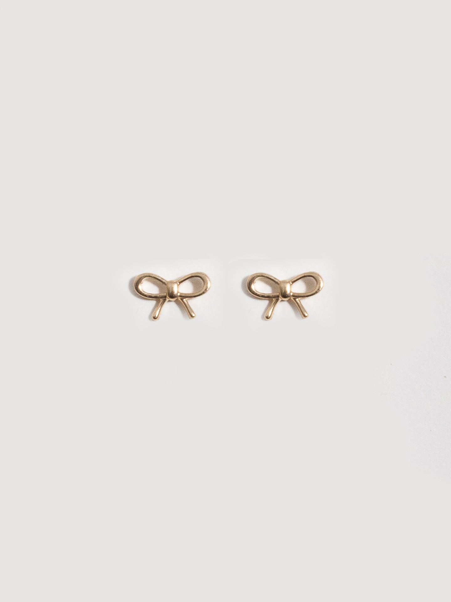 14kt Yellow Gold Mini Bow Studs pictured on light grey background.  