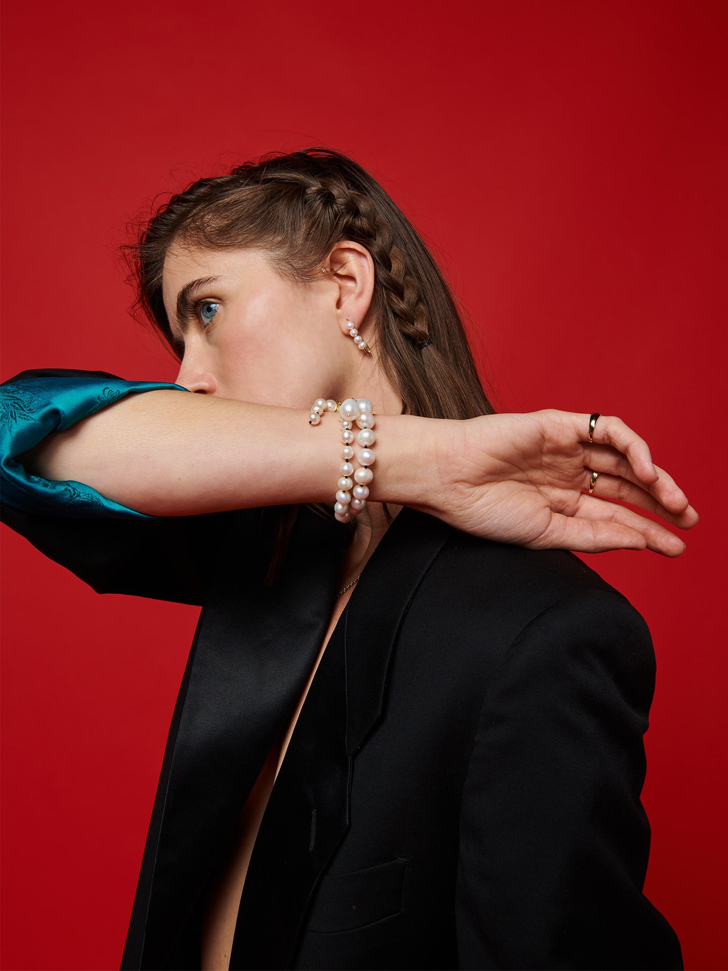14kt Yellow Gold Boujee Pearl Strand pictured as bracelet on models wrist. Red background.