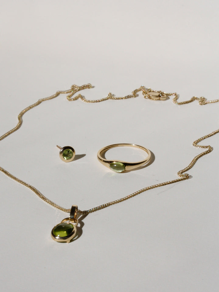 14kt Yellow Gold Peridot Bezel Stud pictured on light grey background with the Mini Gem Signet and Padlock Charm Necklace.