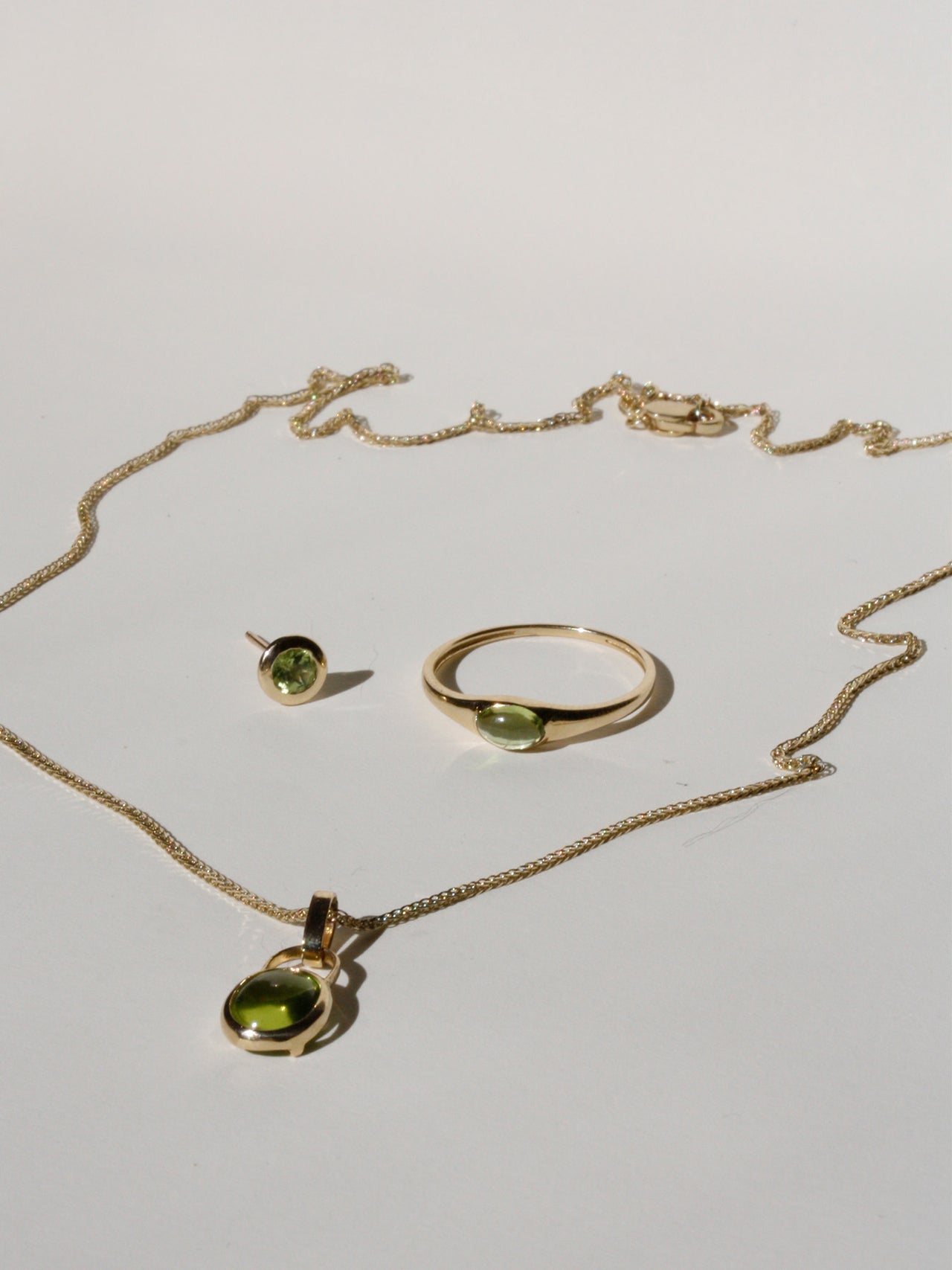 Flat lay of Peridot Mini Gem Signet with the Padlock Charm Necklace and Peridot Bezel Stud on light grey background. 