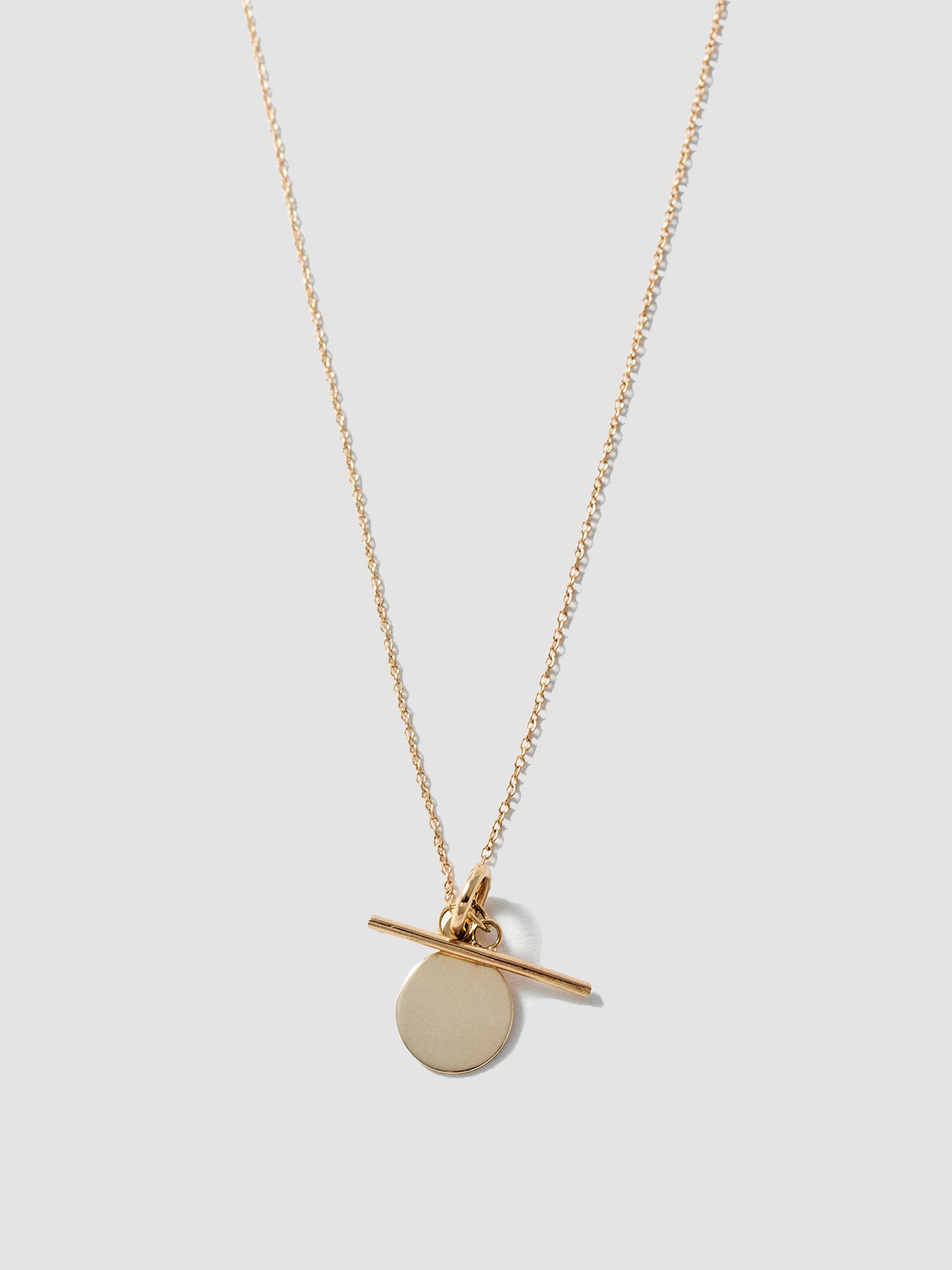 14Kt Yellow Gold Disk and Toggle Necklace pictured on light grey background.