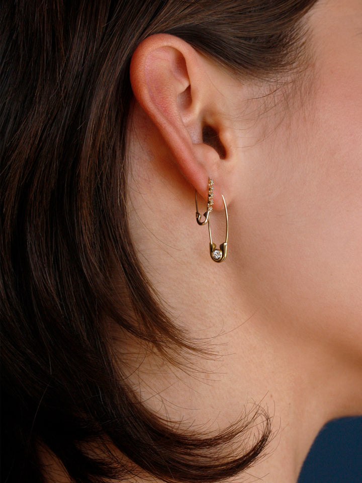 Close-up of an ear wearing a gold hoop earring with a small gemstone.