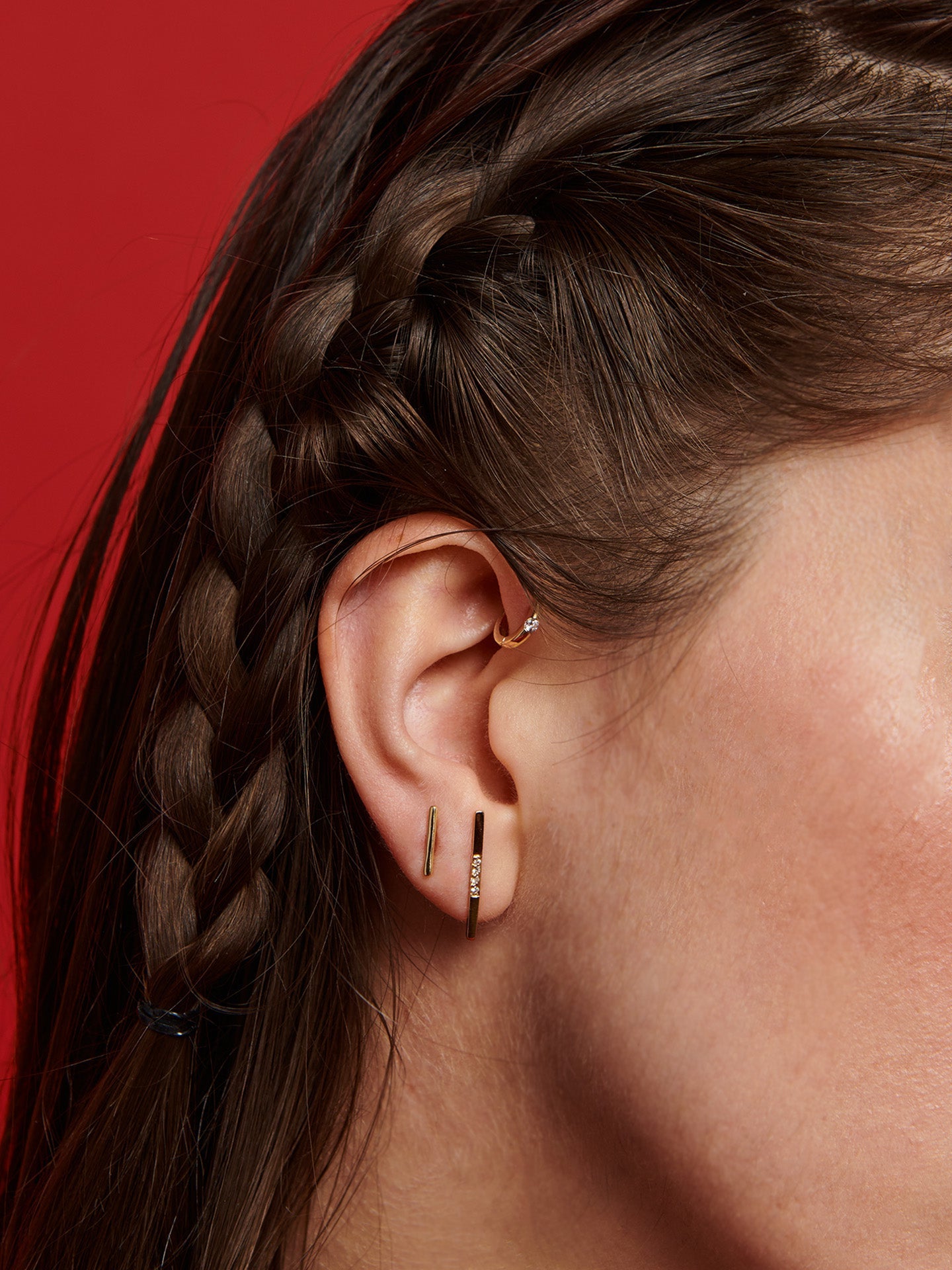 14kt Yellow Gold Rod Stud pictured in models second piercing. Red background.