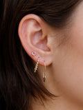 Close-up of an ear wearing gold hoop earrings with gemstones.