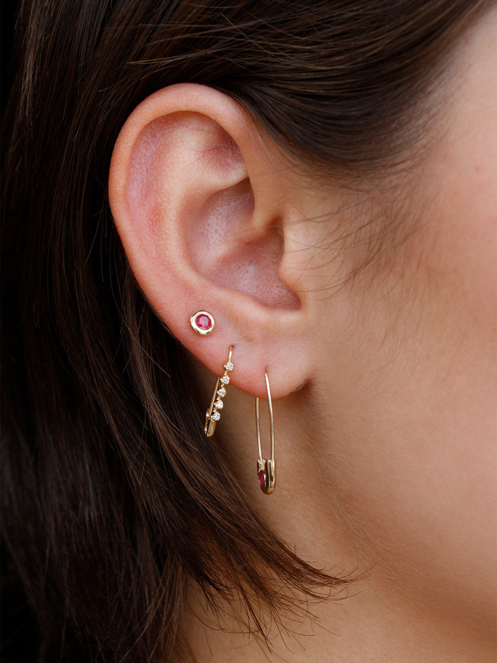 Close-up of an ear wearing gold hoop earrings with gemstones.