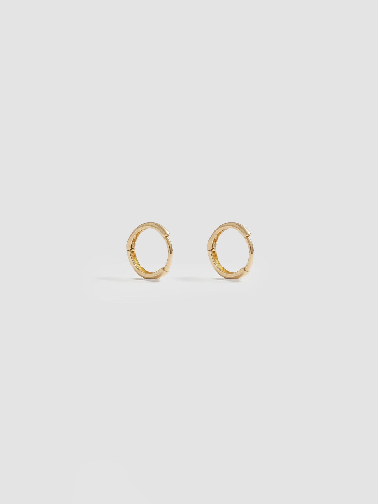 Product shot of the Elfin Mini Huggies (14KT Yellow Gold  8.6mm Diameter 1.4mm Thick) Background: Grey backdrop