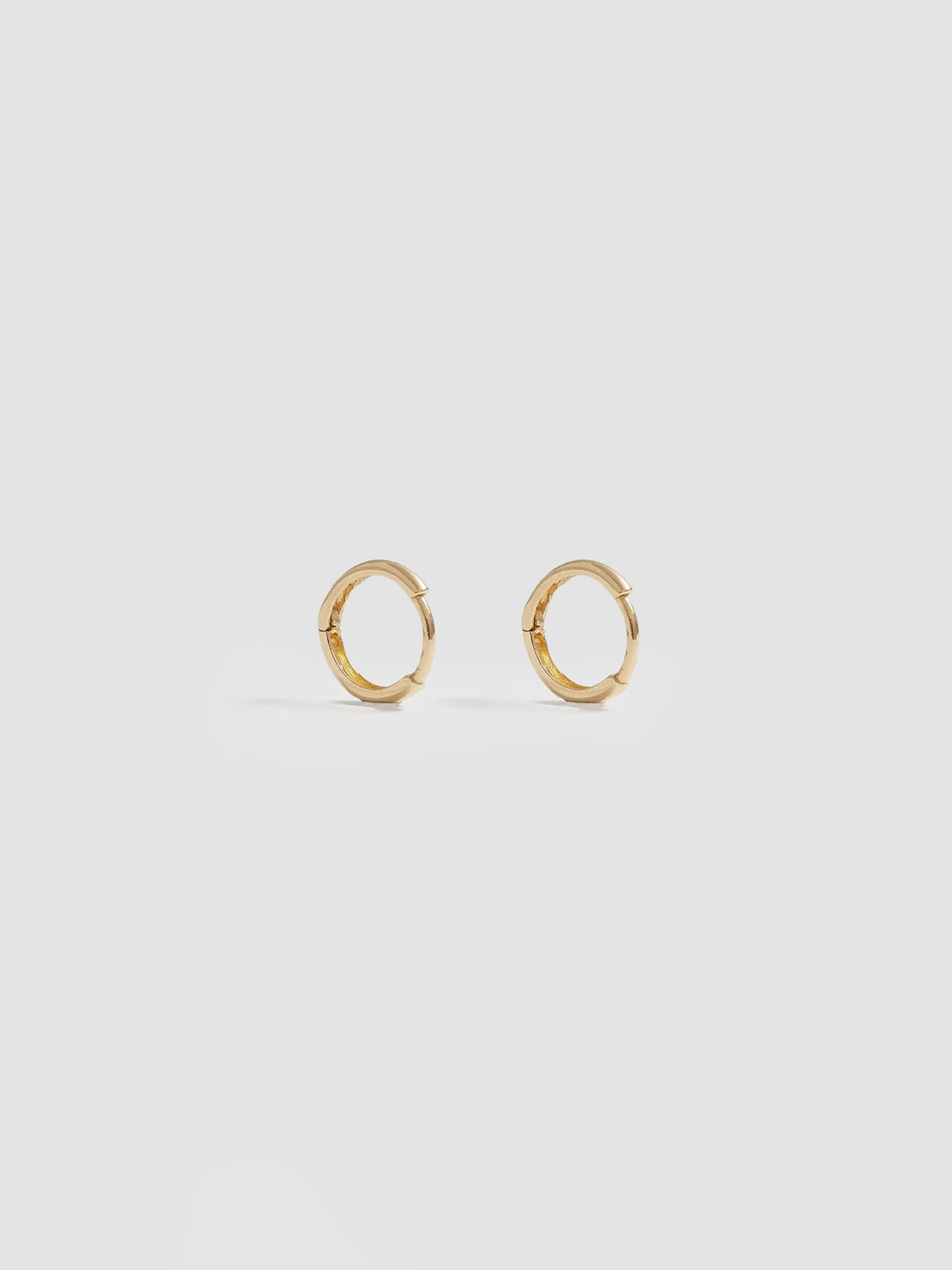 Product shot of the Elfin Mini Huggies (14KT Yellow Gold  8.6mm Diameter 1.4mm Thick) Background: Grey backdrop